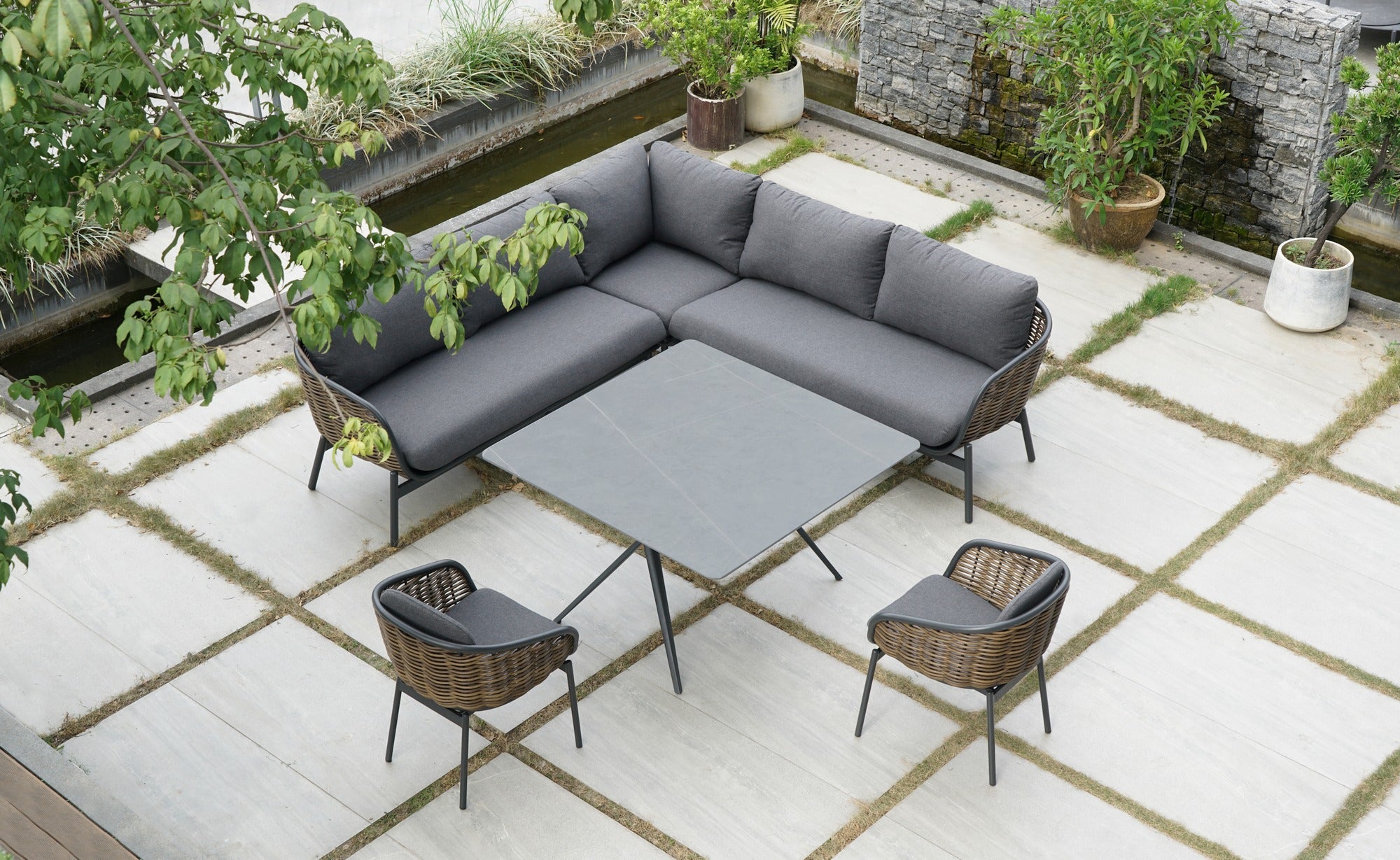 Die Garten Eckbankgruppe 'Claire' mit braun meliertem Kunststoffgeflecht, dunkelgrauen Kissen und einem Sinterstone-Tisch in Marmoroptik, angeboten von Gartenmöbelshop.at.